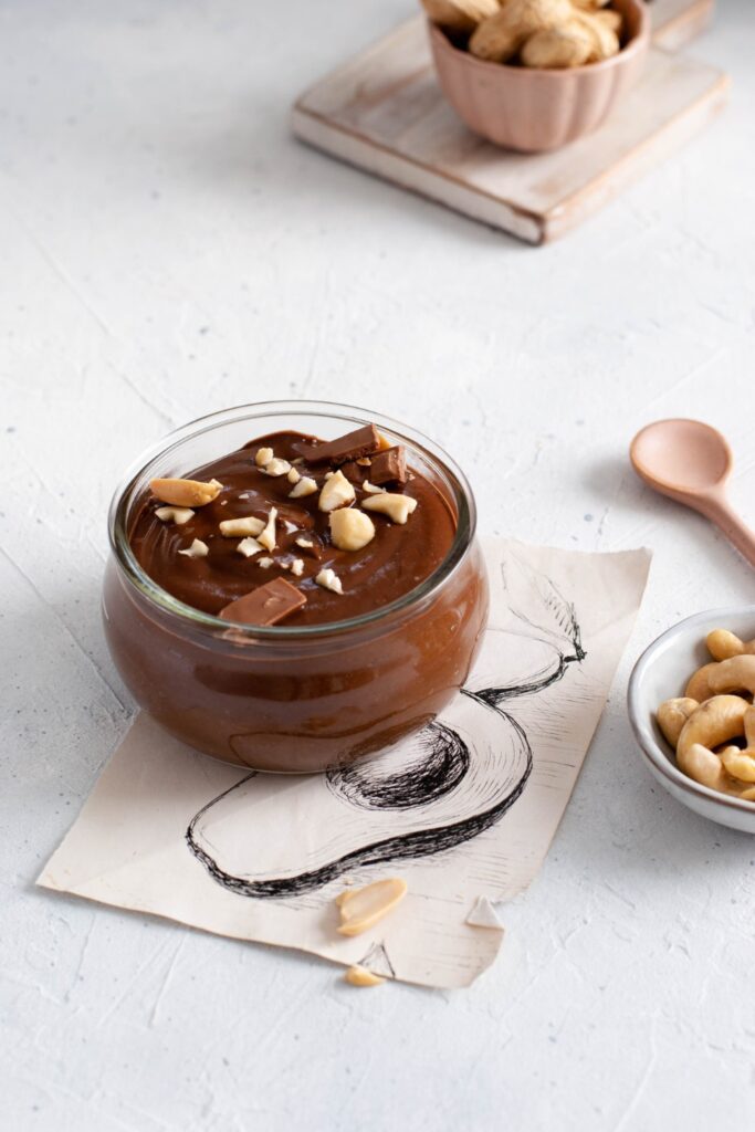 Chocolate rice pudding in a glass bowl with cashews and a wooden spoon.