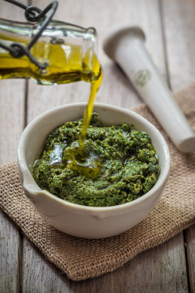 Bowl of Giada De Laurentiis Arugula Pesto with olive oil being poured in.