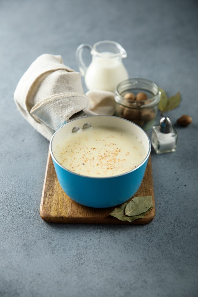 Pot of bechamel sauce with milk and spices on a wooden board.