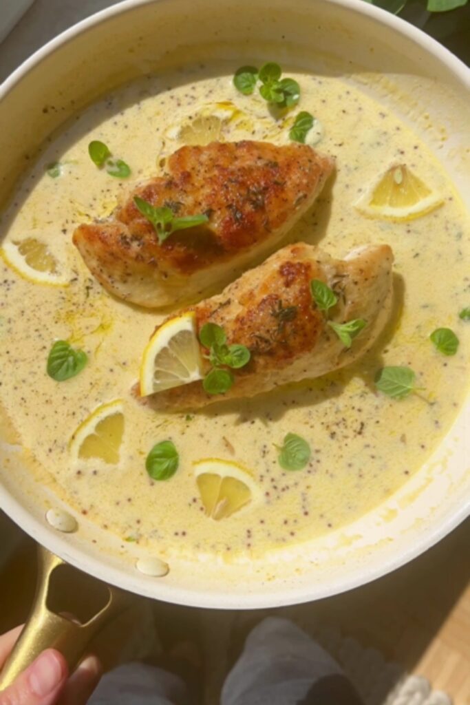 Chicken Francese in a skillet with lemon slices and fresh herbs.