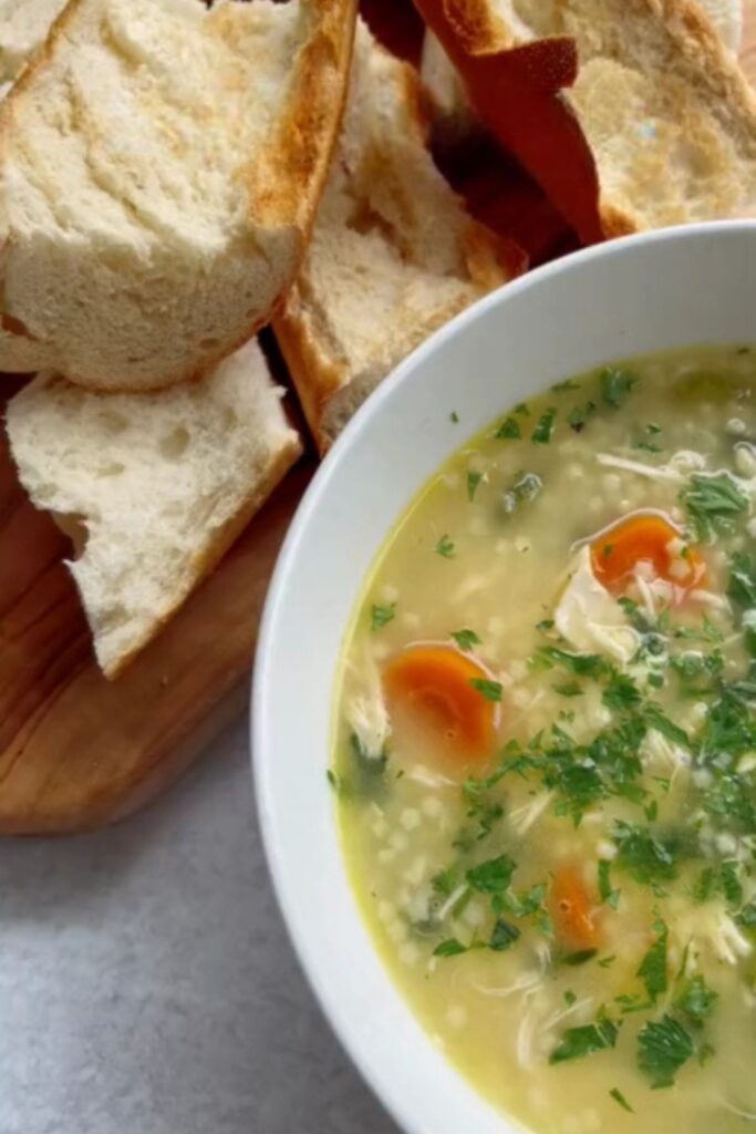 Giada De Laurentiis Chicken Pastina soup in a white bowl with bread slices.