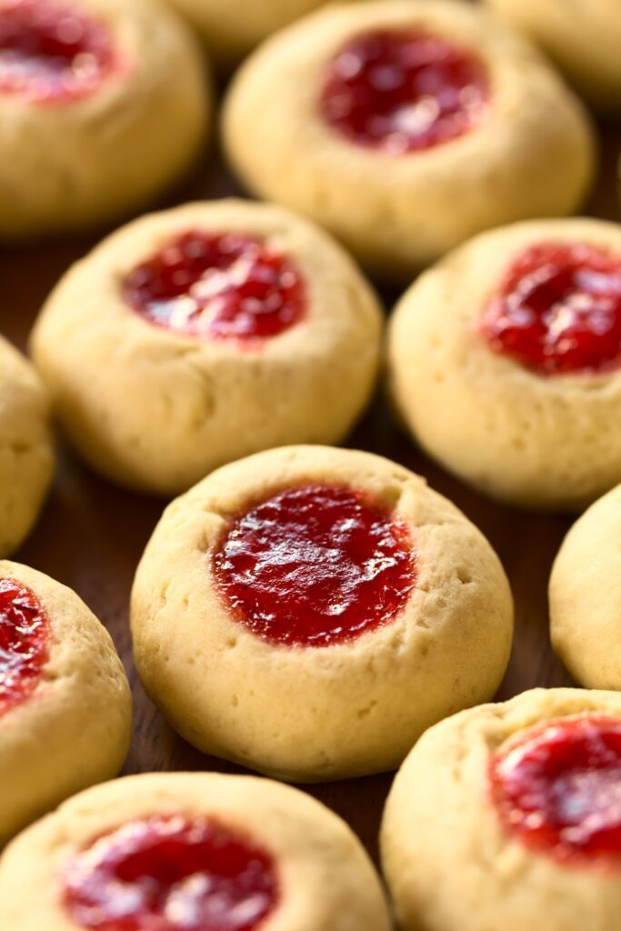 Giada Cherry Almond Thumbprint Cookies on a wooden tray with a jar of cherry jam.