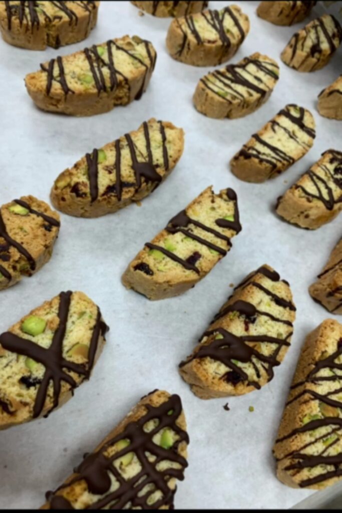 Cherry-pistachio biscotti drizzled with chocolate on parchment paper.