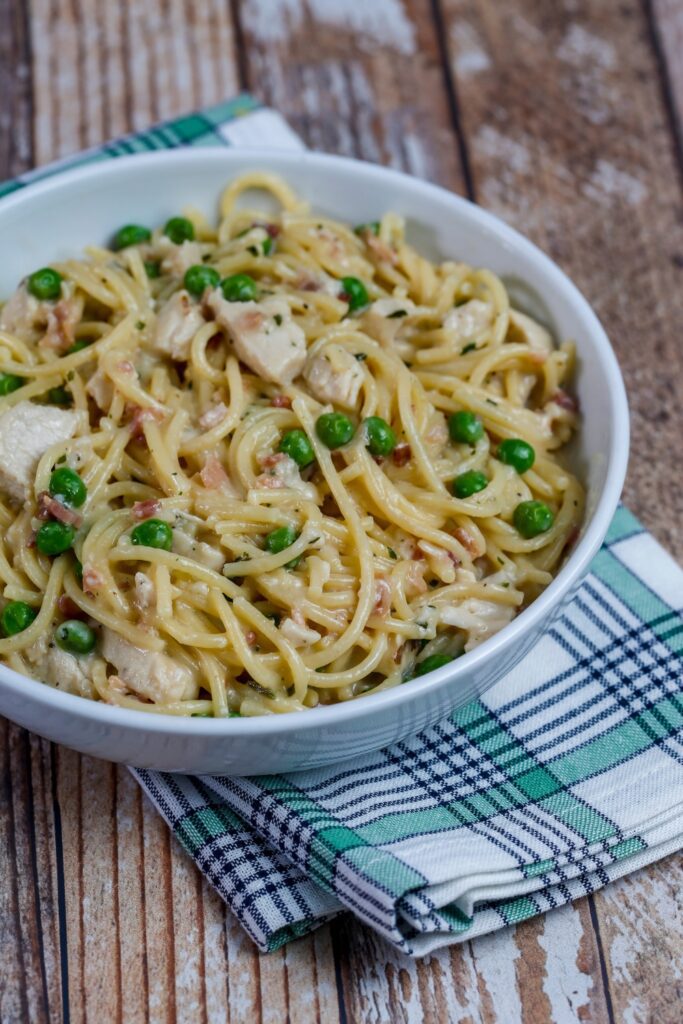 Bowl of chicken carbonara with peas on a plaid napkin.