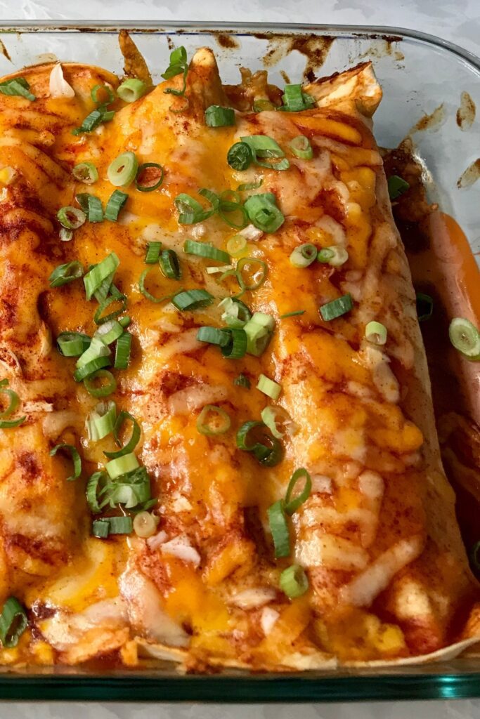 Chicken Enchiladas in a baking dish topped with melted cheese and green onions.