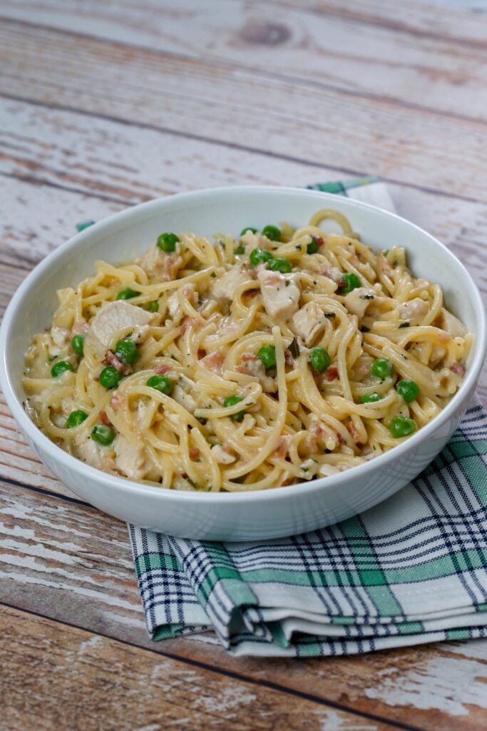 Chicken carbonara with peas in a bowl on a wooden surface.