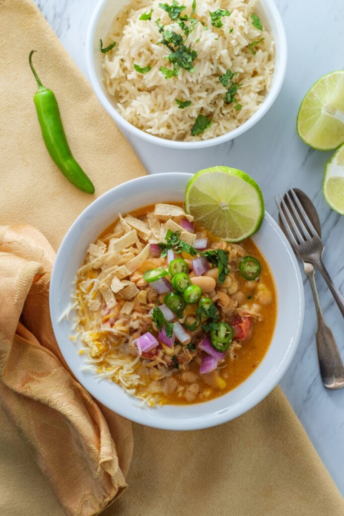 Bowl of white bean and chicken chili garnished with fresh lime and cilantro, served with rice.