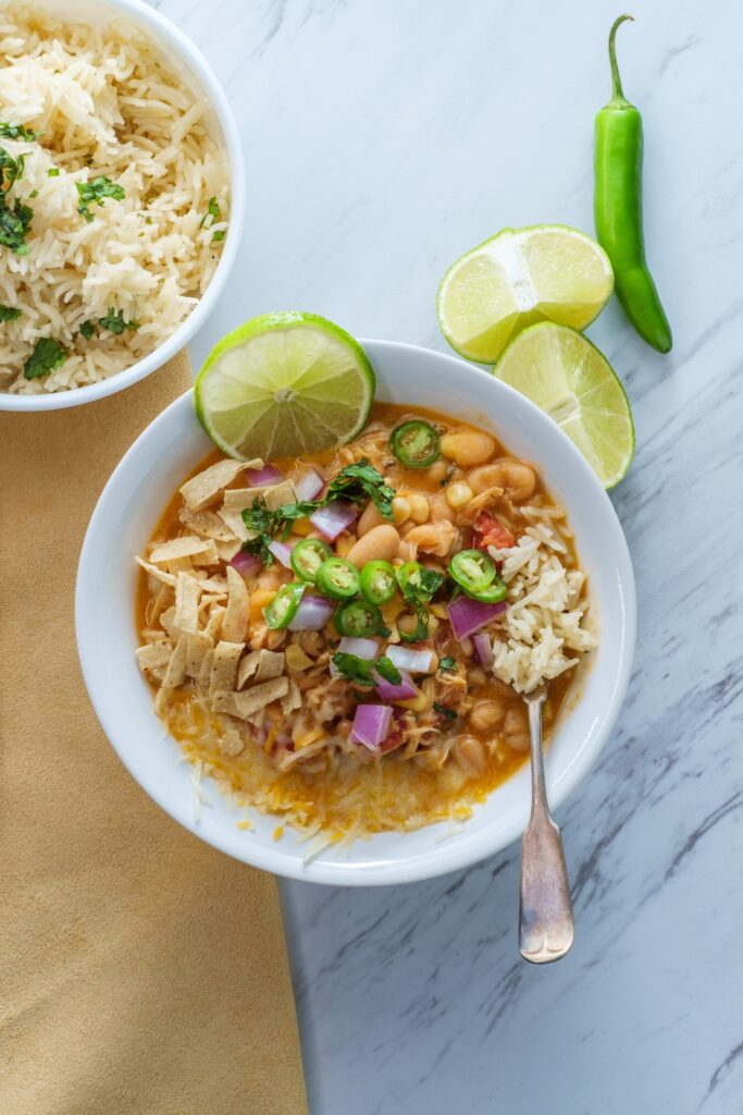 Bowl of white bean and chicken chili with rice and lime wedges on the side.