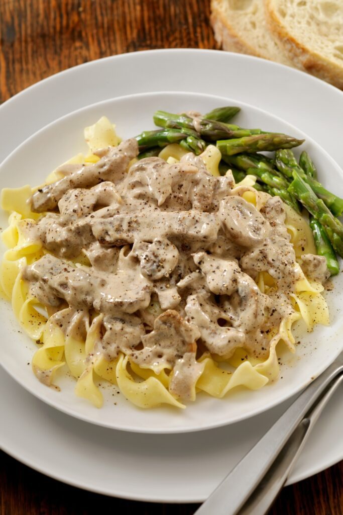 Giada De Laurentiis beef stroganoff with noodles and asparagus on a plate.