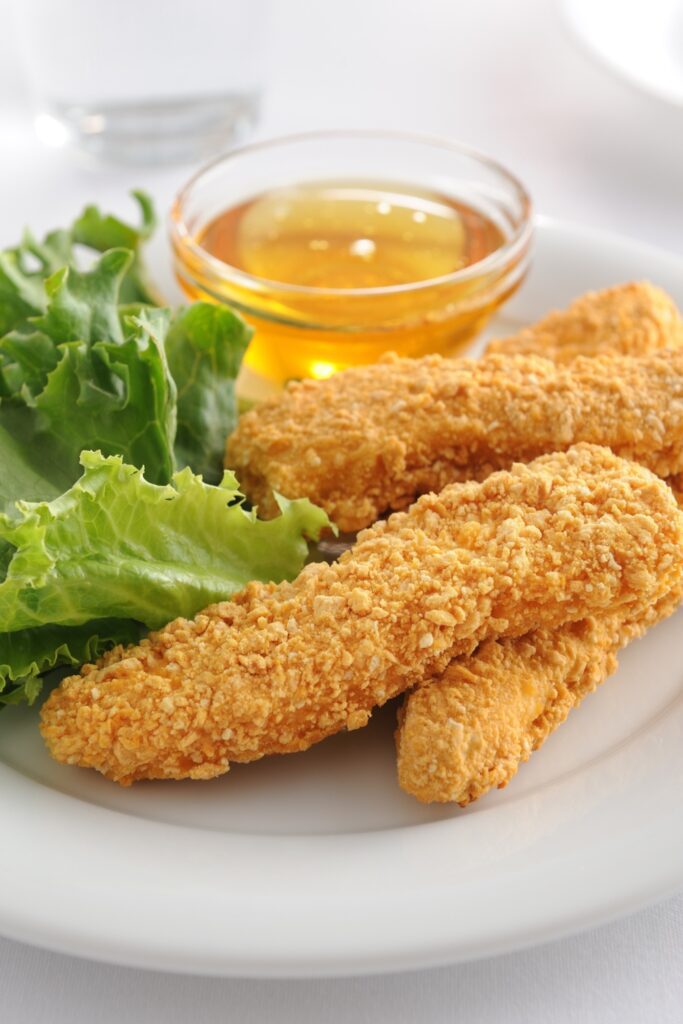 Giada Crunchy Parmesan Chicken Tenders with honey dip and lettuce on a white plate.