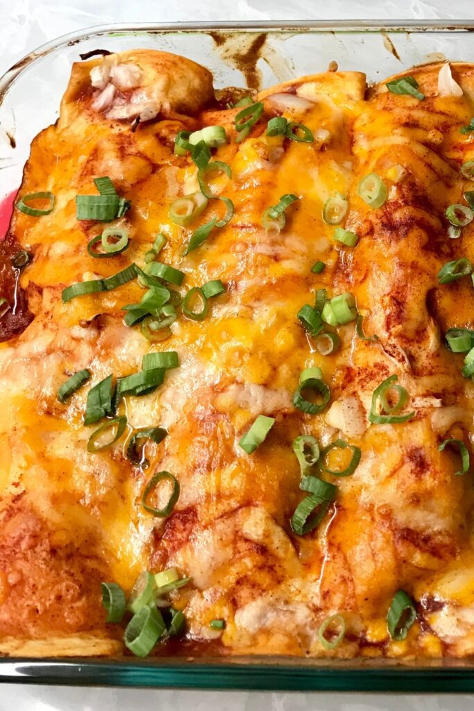 Chicken Enchiladas in a baking dish with cheese and green onions.