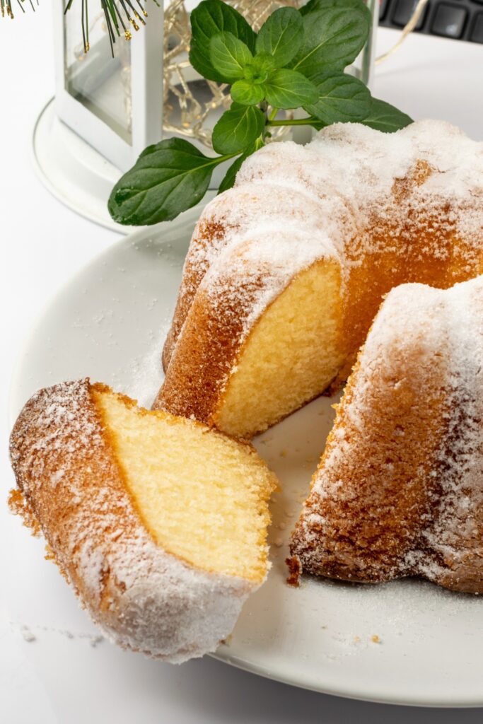 Whole Ciambella cake with a slice on a white plate, dusted with powdered sugar.