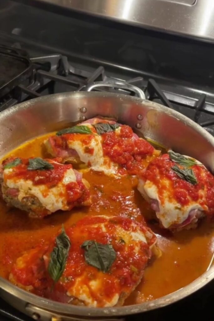 Giada De Laurentiis Chicken Sorrentino with tomato sauce and basil leaves in a pan.