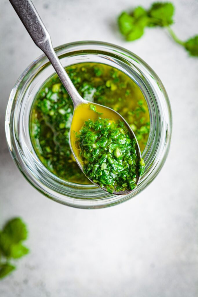 Spoonful of Giada De Laurentiis chimichurri sauce held over a jar of the sauce.