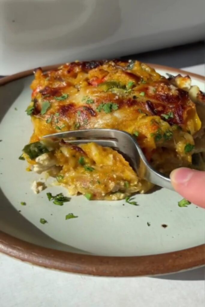 A fork cutting into a slice of butternut squash lasagna on a plate.