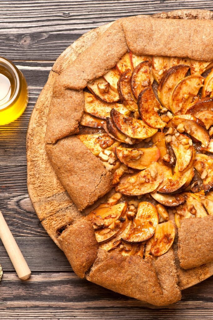 apple crostata with a golden-brown crust and sliced apples, served with honey on a wooden board.