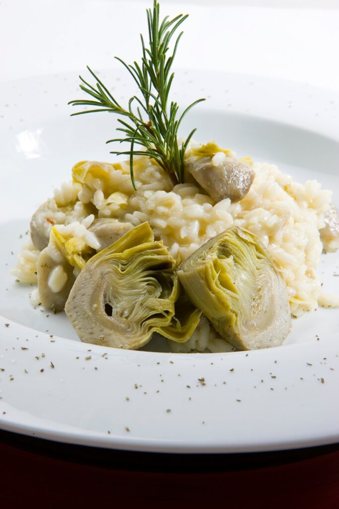 Artichoke risotto garnished with fresh rosemary, served on a white plate.