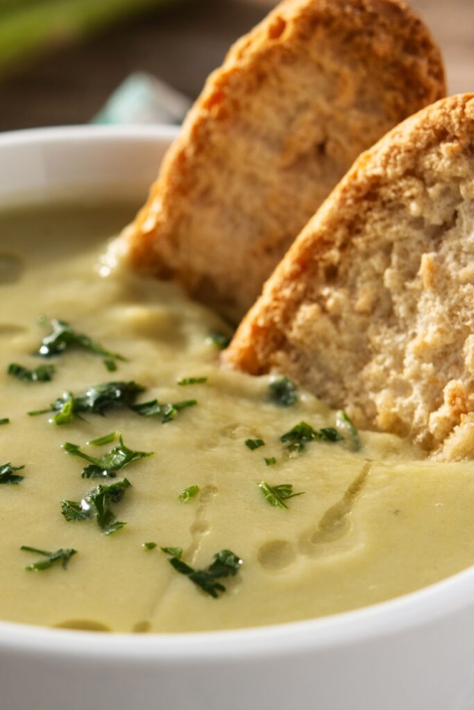 asparagus soup garnished with herbs, with toasted bread slices dipped into the soup.