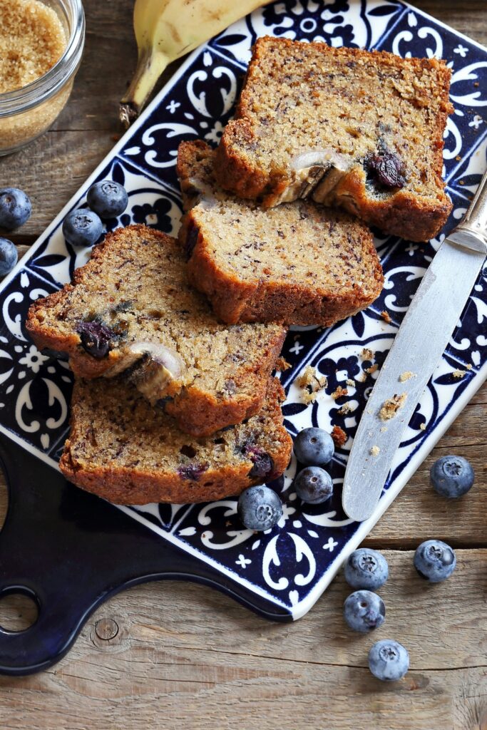 Slices of blueberry-banana bread on a decorative plate with fresh blueberries.