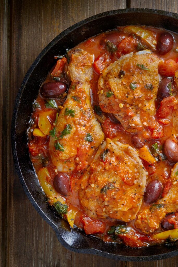 chicken cacciatore in a cast iron skillet on a wooden table.