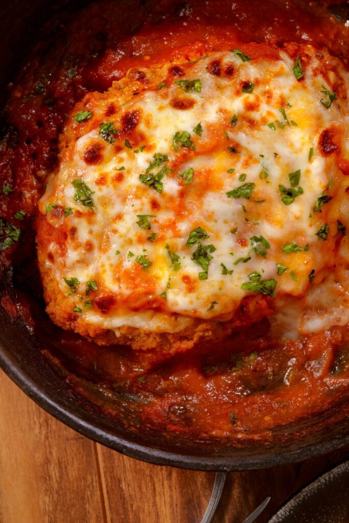 chicken Parmesan topped with melted cheese and fresh parsley in a skillet.