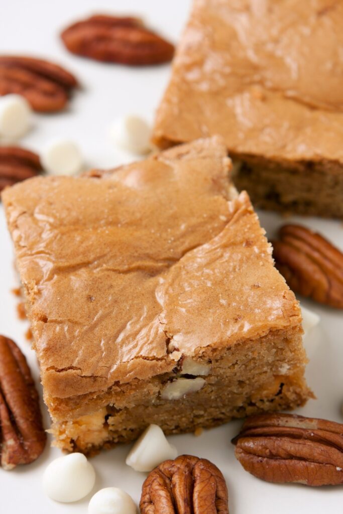 Chocolate peanut butter blondies with pecans and white chocolate chips on a plate.