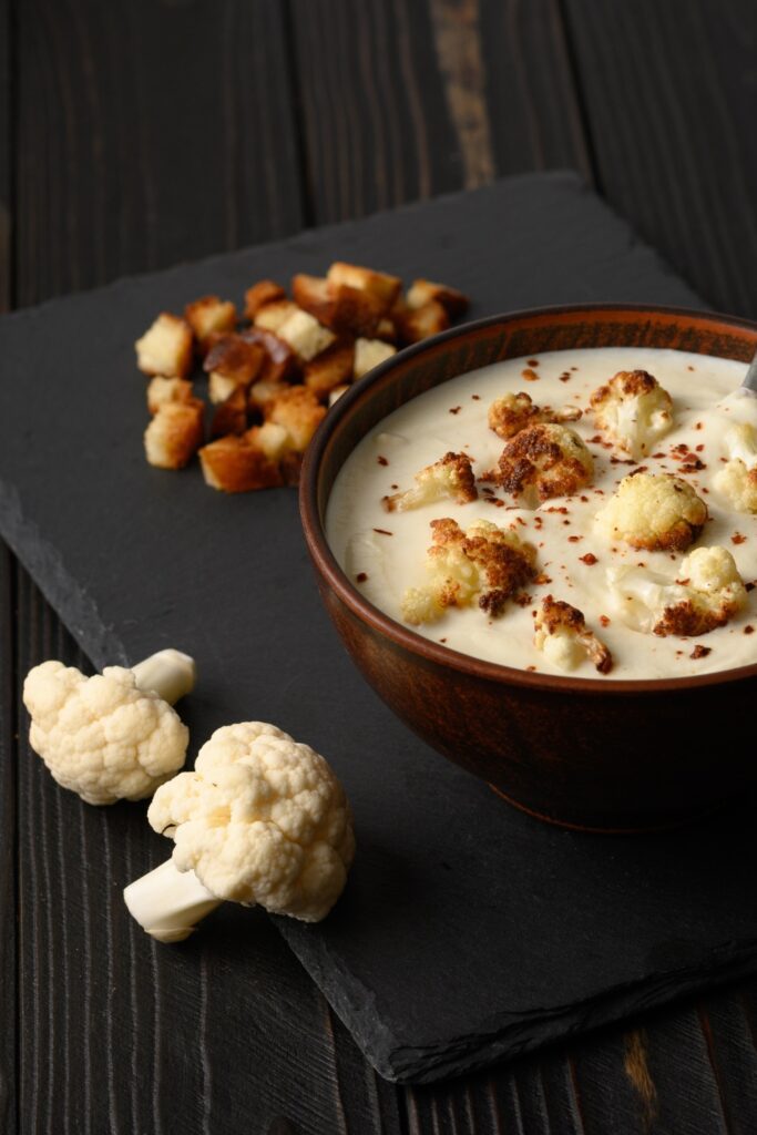 Giada Cold Cauliflower Soup with roasted cauliflower and croutons, surrounded by walnuts on a dark wooden table.