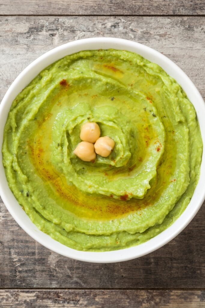 A bowl of Giada Avocado Hummus with chickpeas on top, drizzled with olive oil.