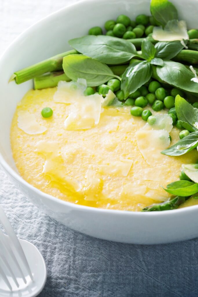 Giada De Laurentiis Cheesy Polenta topped with peas, asparagus, and basil, served in a white bowl.