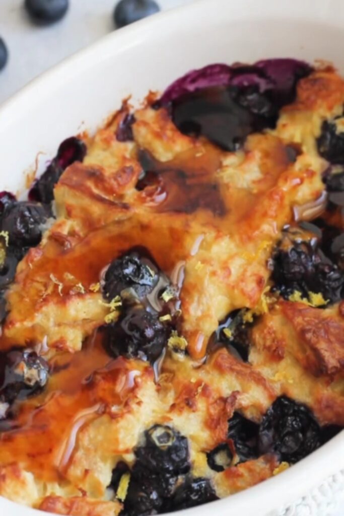 Giada Baked Blueberry French Toast Casserole drizzled with syrup in a white baking dish.