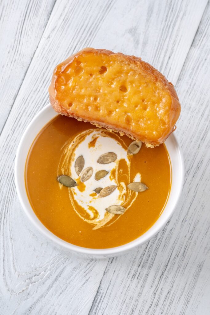 A bowl of Giada Butternut Squash Soup with Fontina cheese crostini resting on the edge.