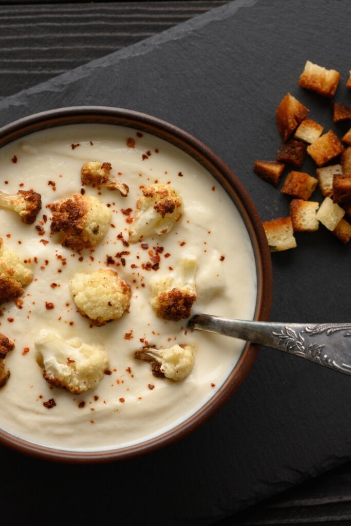 Giada Cold Cauliflower Soup with roasted cauliflower and croutons in a brown bowl on a dark slate.