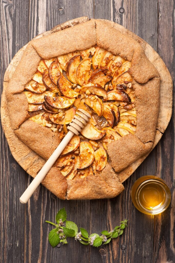 Apple crostata with golden-brown crust and apple slices, topped with honey, on a wooden board.