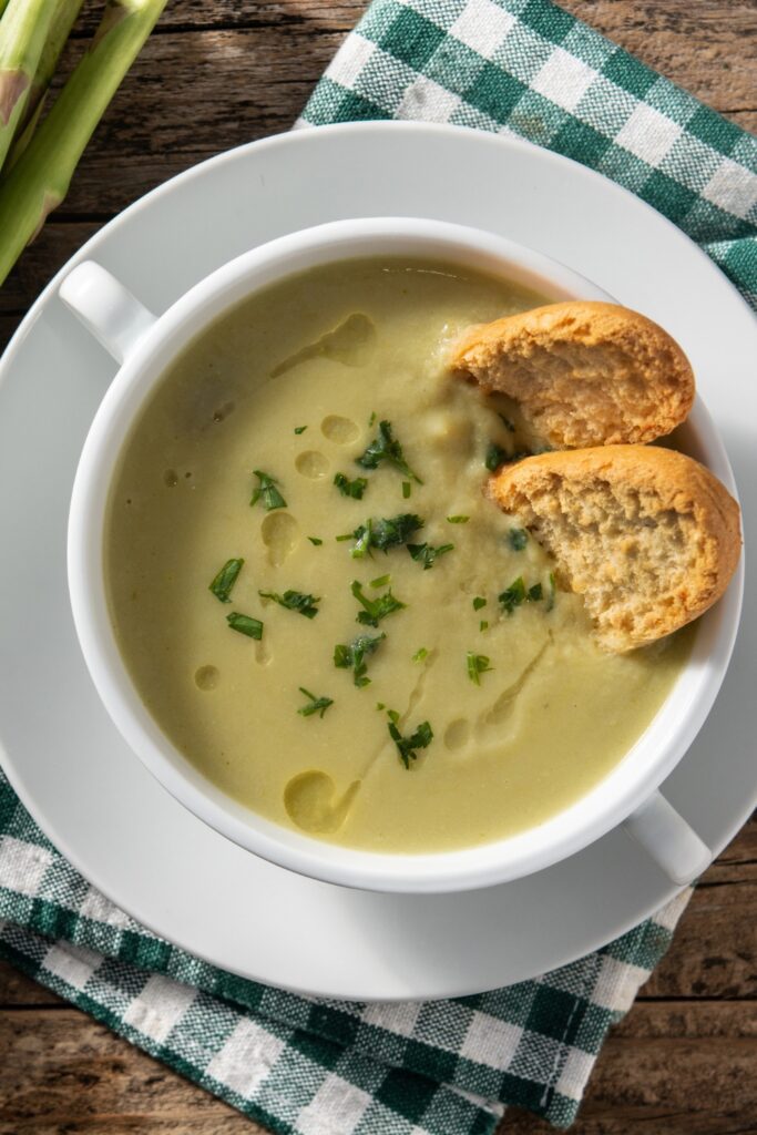 Bowl of asparagus soup topped with fresh herbs and served with toasted bread slices.