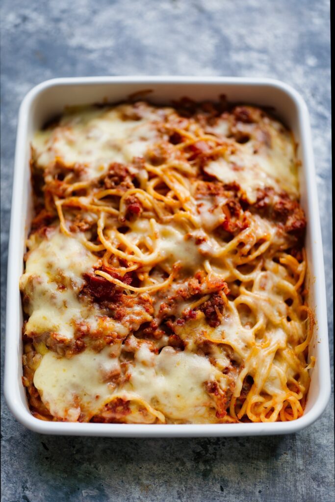 Baked Bolognese with melted cheese in a white dish on a blue cloth.