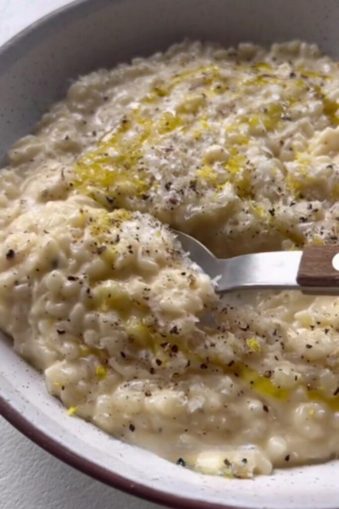 A bowl of Giada De Laurentiis Basic Risotto, topped with grated Parmesan, black pepper, and a drizzle of olive oil.