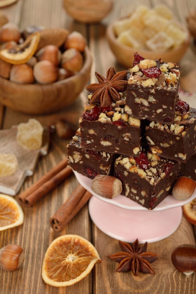 Stack of chocolate fudge pieces topped with nuts and dried fruit, surrounded by dried orange slices and nuts.