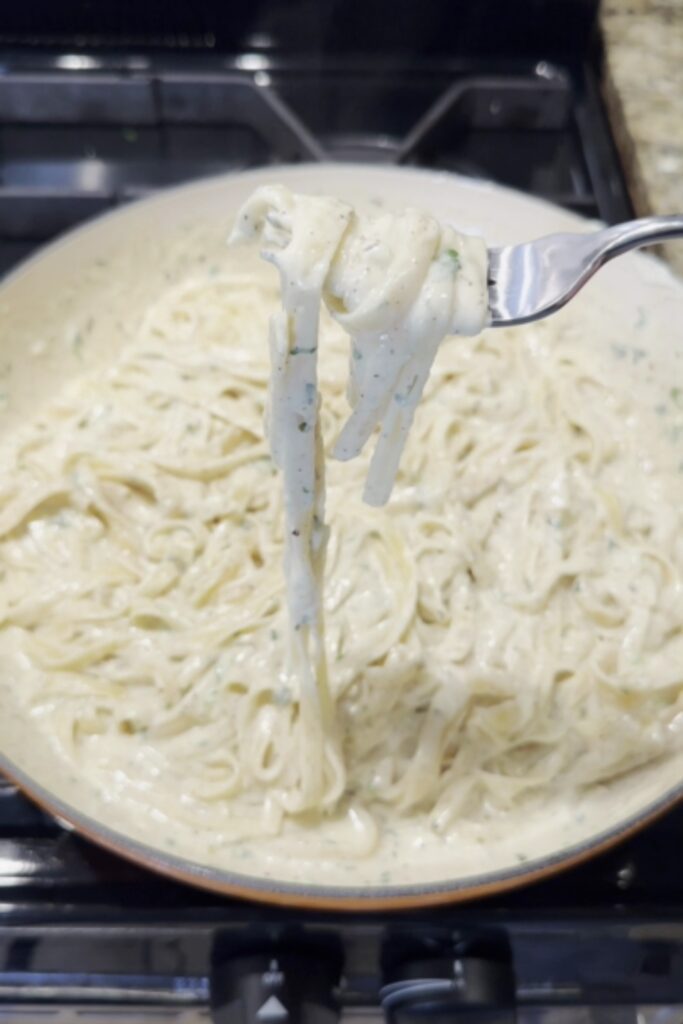 A fork lifting a creamy strand of fettuccine from a pan of Giada De Laurentiis Fettuccine Alfredo.