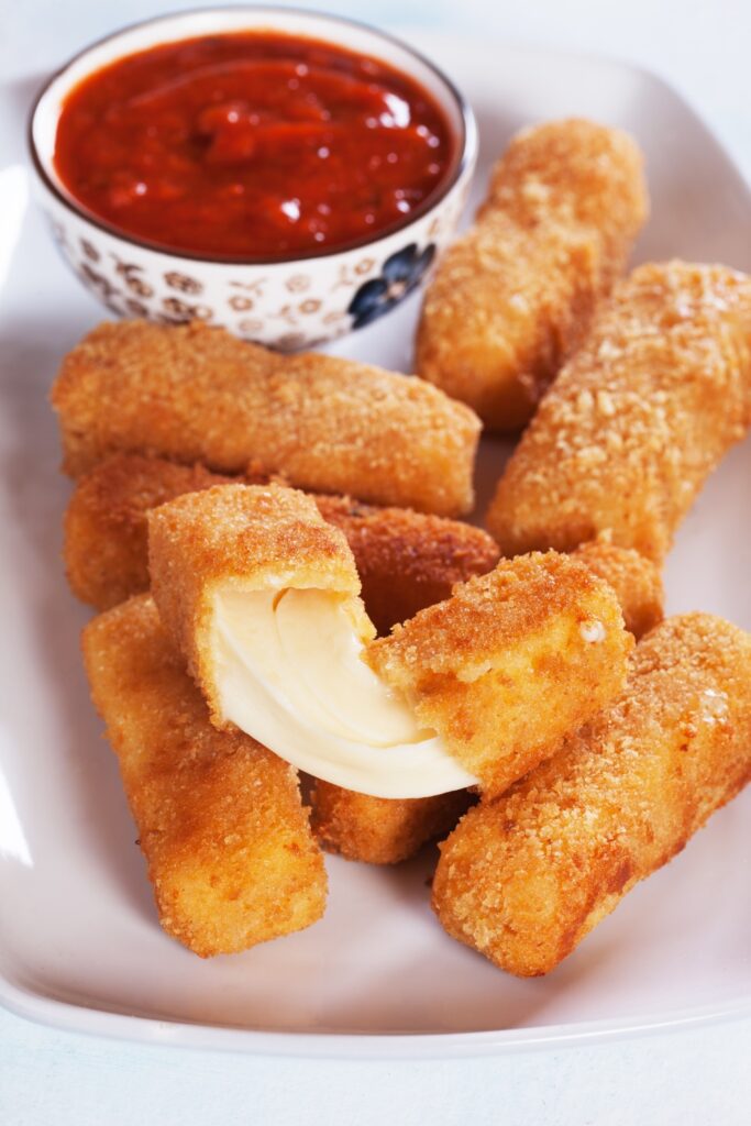 Giada De Laurentiis Mozzarella Cheese Sticks with marinara sauce in a black bowl on a green plate.