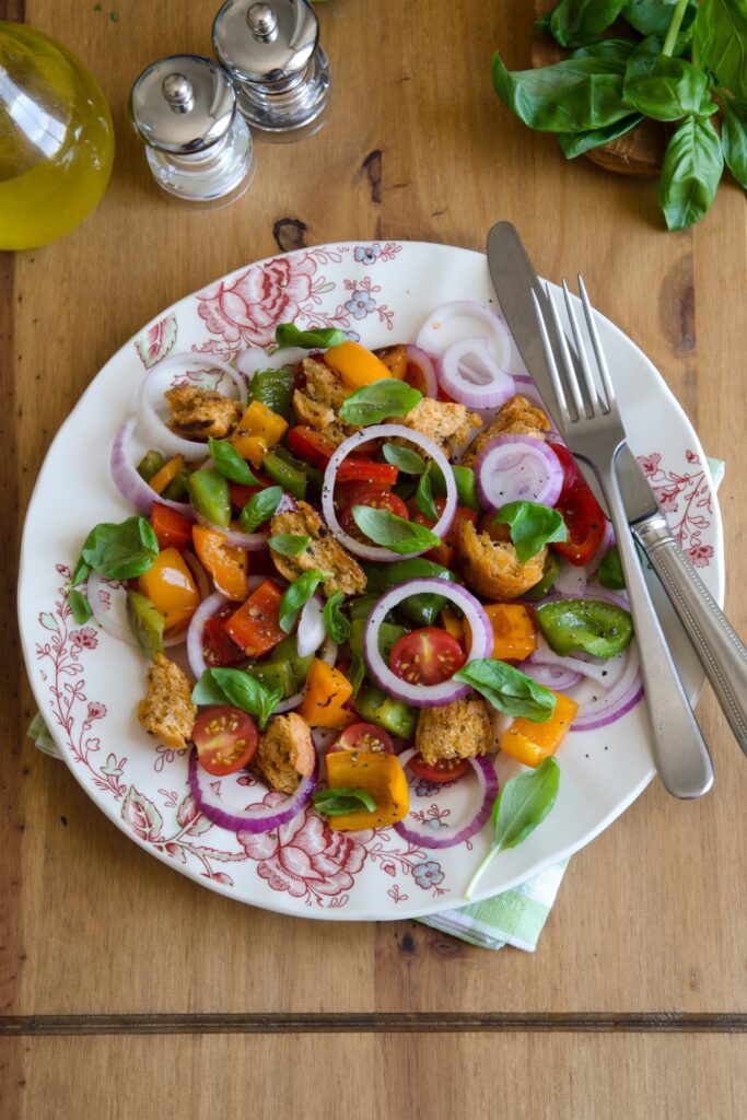 Colorful panzanella salad with tomatoes, bell peppers, red onions, and croutons on a floral plate.