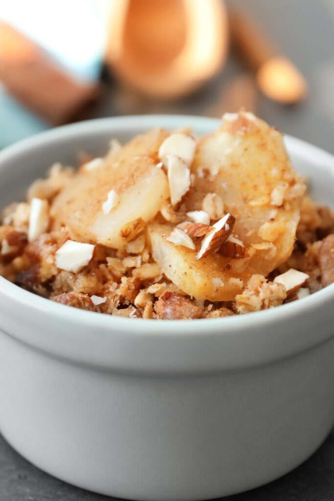 Vegan apple crisp topped with sliced apples and nuts in a white bowl.