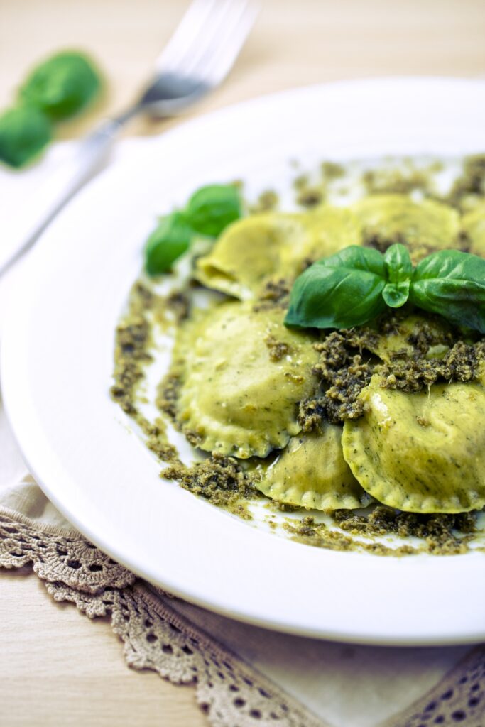 Ravioli with herb pesto and fresh basil on a white plate.
