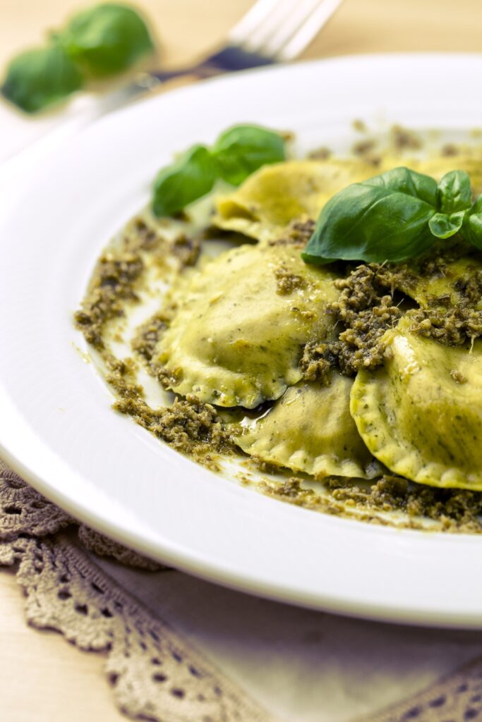 Four-cheese ravioli with herb pesto and basil leaves on a white plate.