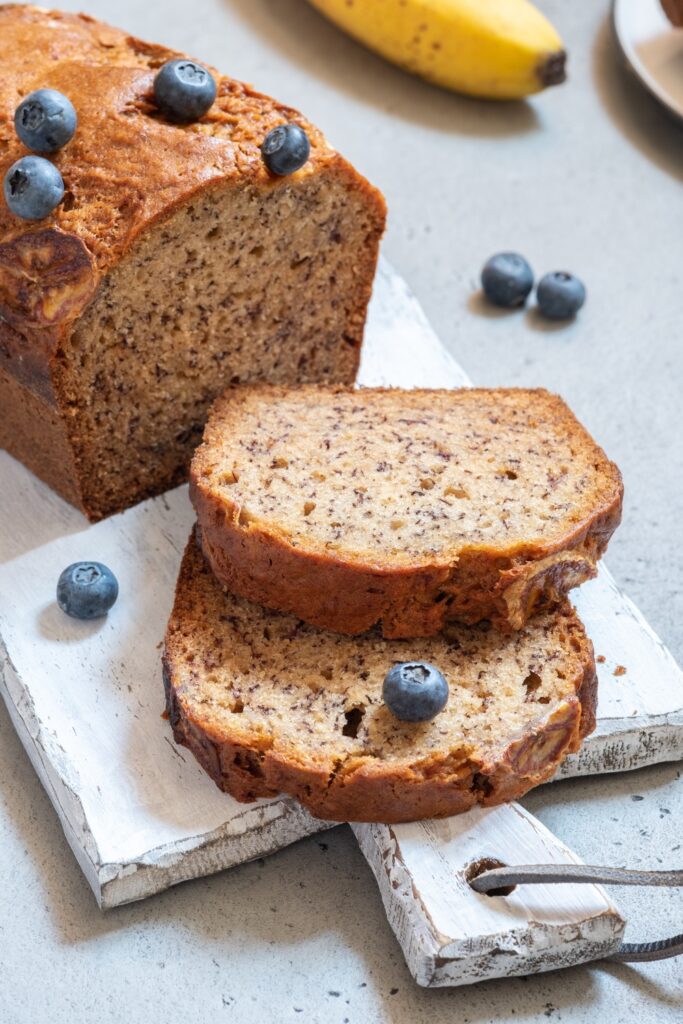 Sliced blueberry-banana bread on a white cutting board, topped with fresh blueberries.