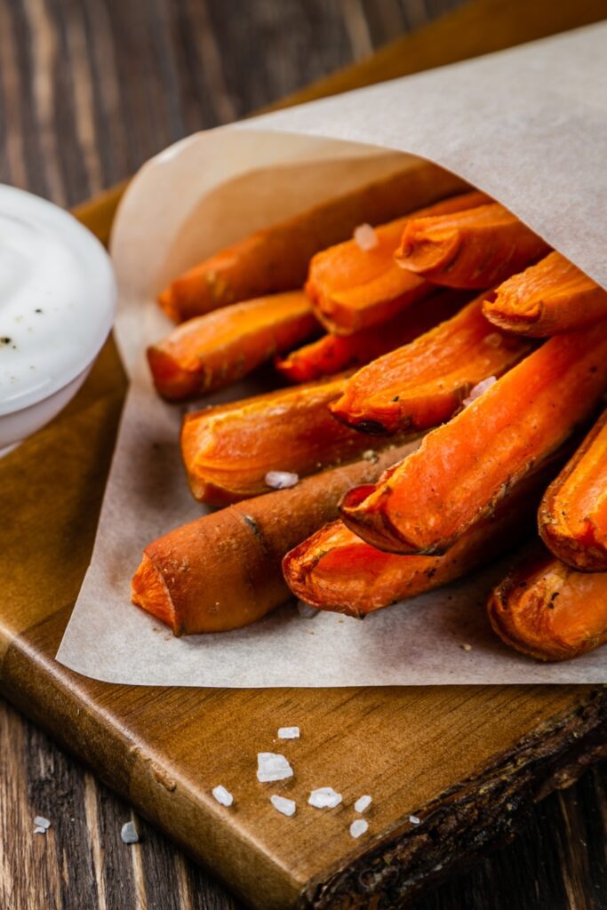 Crispy carrot fries wrapped in parchment paper with sea salt on a wooden board