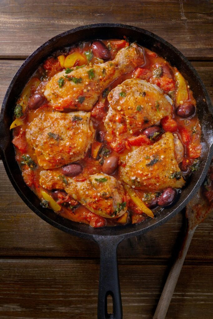 Chicken cacciatore with tomatoes, bell peppers, and olives in a cast iron skillet.