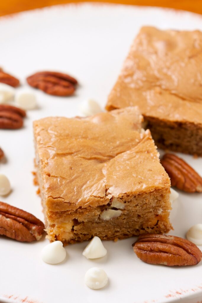 Two chocolate peanut butter blondies on a plate with pecans and white chocolate chips.