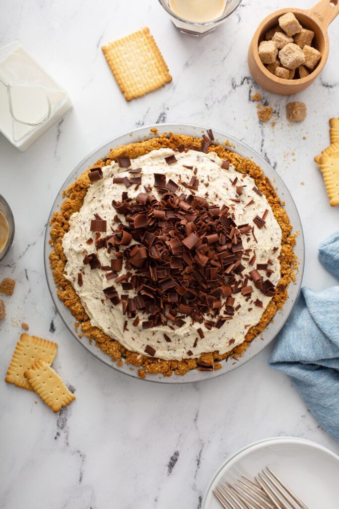 Whole chocolate ricotta cheesecake with chocolate shavings on a marble surface.