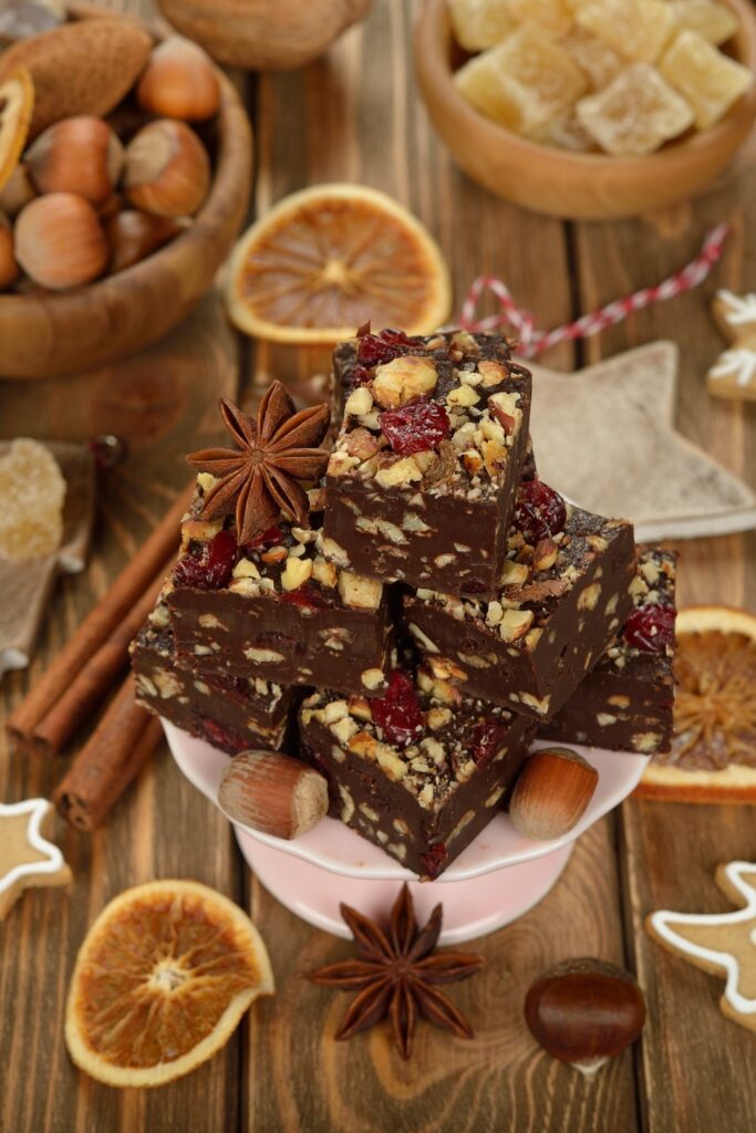 Cinnamon chocolate fudge pieces on a pink stand, surrounded by nuts and dried fruits.