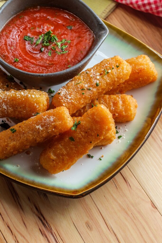 Giada De Laurentiis Mozzarella Cheese Sticks with marinara sauce in a white bowl, cheese stretching out from one stick.